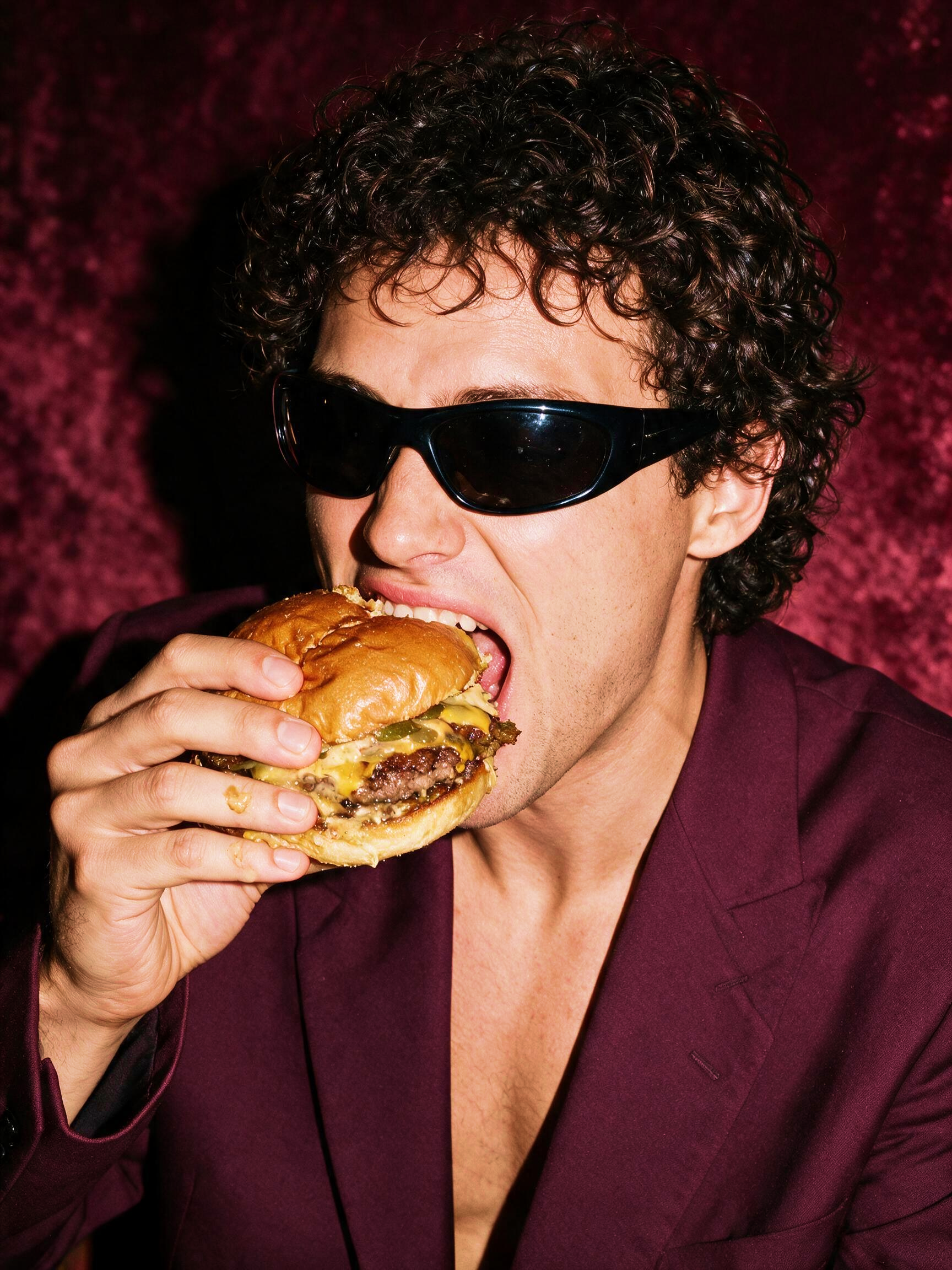 A guest in sunglasses taking a bite of a shareable cheeseburger