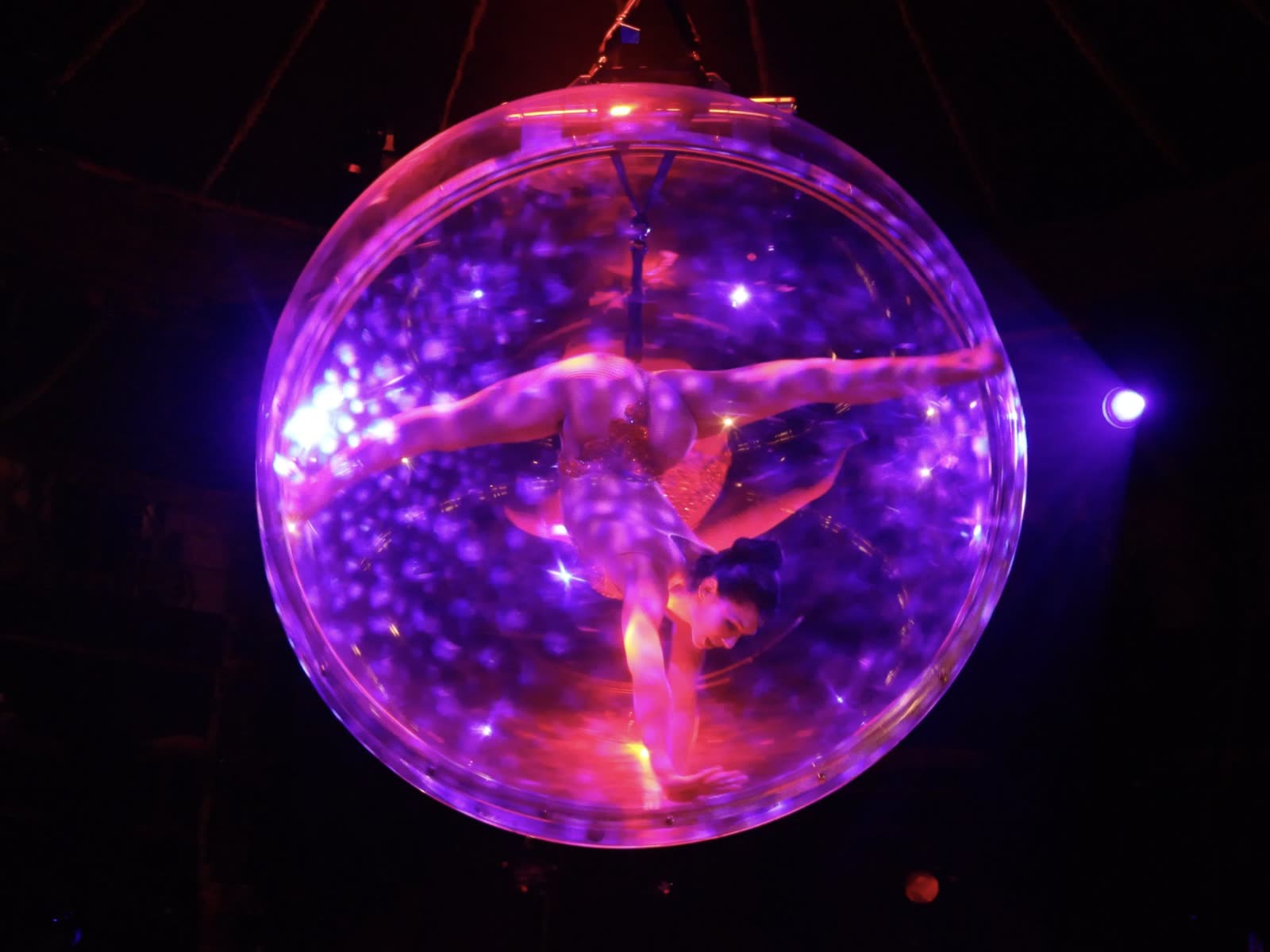 Aerialist in a split inside a glowing purple sphere.